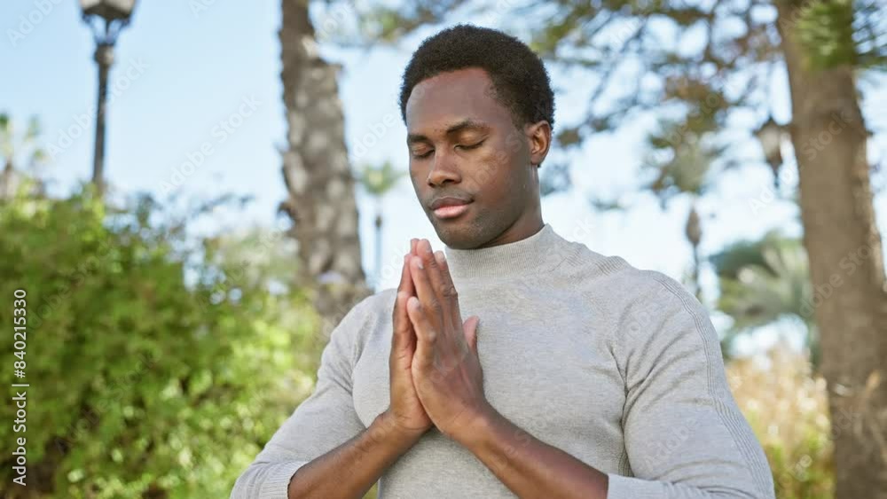 A contemplative young black man with folded hands enjoys tranquil moments in a lush park. A contemplative young black man with folded hands enjoys tranquil moments in a lush park.