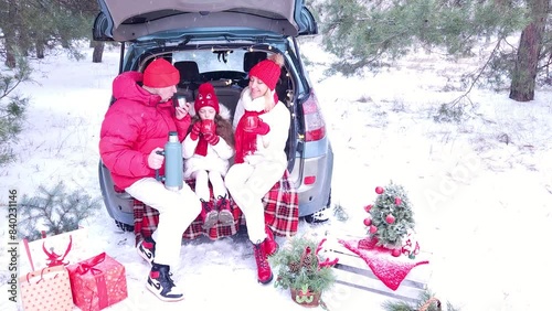 Family - father, mother and daughter cheerfully celebrate Christmas in the forest, sitting in the trunk of a car, drinking hot tea