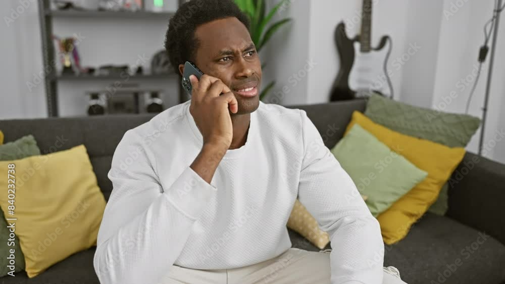 A cheerful man in casual attire talks on a smartphone, comfortably seated on a sofa in a modern living room. A cheerful man in casual attire talks on a smartphone, comfortably seated on a sofa in a modern living room.