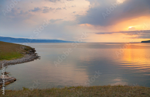 Beautiful morning landscape of Baikal Lake in summer with rising sun over Olkhon Island and reflection of sunrise in calm water. Scenic view of Small Sea. Natural background. Summer travels