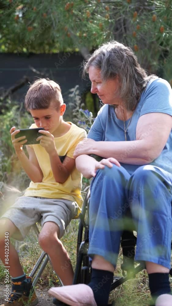 Grandmother in wheelchair looking at cell phone with her grandson outdoors Grandmother in wheelchair looking at cell phone with her grandson outdoors