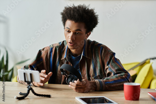 A young African American man sits at a table, engaging with a phone and tripod while talking. photo