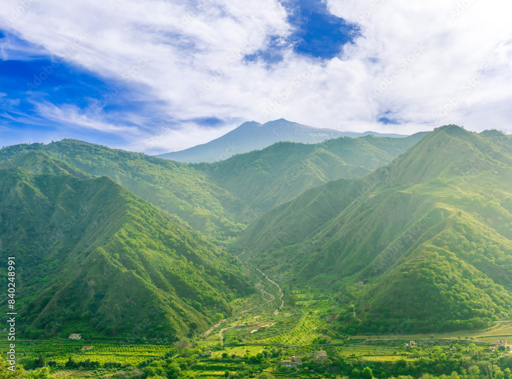 Fototapeta premium amazing view at a green landscape between two mountains with a high peak with snow and blue cloudy sky on background