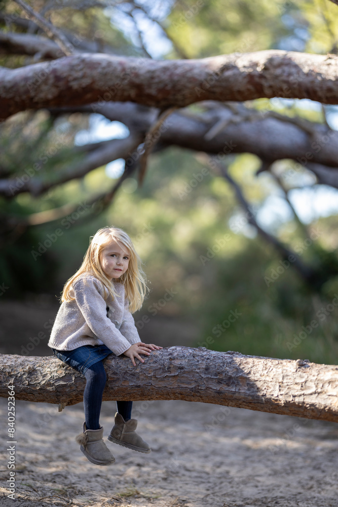 Lovely blonde little girl sitting on a tree trunk in the forest