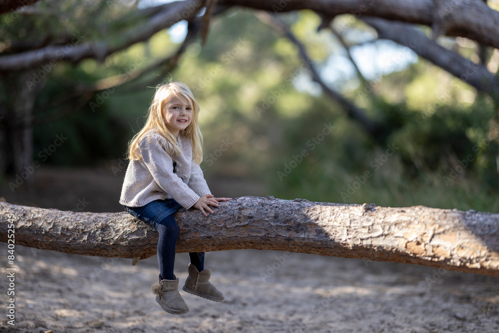 Lovely blonde little girl sitting on a tree trunk in the forest
