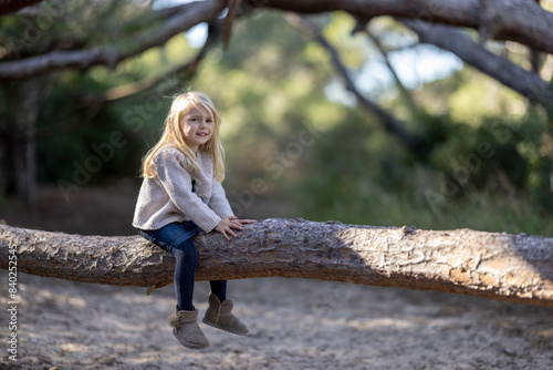 Lovely blonde little girl sitting on a tree trunk in the forest