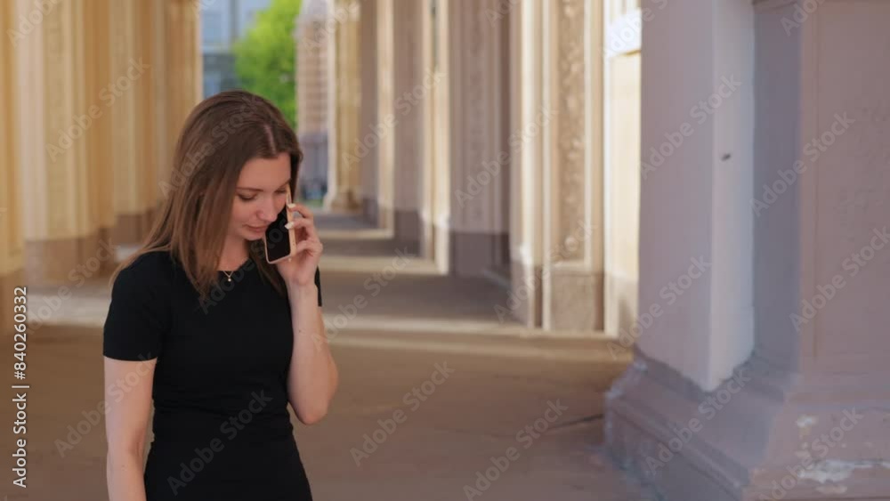 Chatting phone, Stylish conversation, Elegant dress. Young woman in black dress is having conversation on her smartphone while standing in ornate outdoor corridor adorned with decorative columns. Chatting phone, Stylish conversation, Elegant dress. Young woman in black dress is having conversation on her smartphone while standing in ornate outdoor corridor adorned with decorative columns.