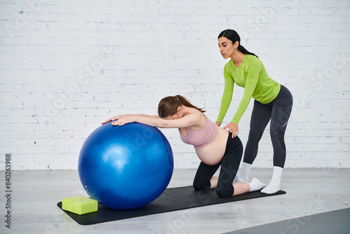 A pregnant woman is doing exercises on an exercise ball with her coach during parents courses.