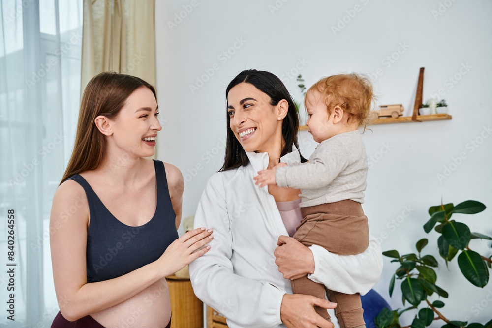 A young, beautiful mother holds her baby while smiling at her supportive coach during a parents course at home. A young, beautiful mother holds her baby while smiling at her supportive coach during a parents course at home.