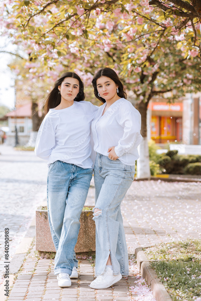 Two women are posing for a picture in front of a tree. They are wearing jeans and white shirts Two women are posing for a picture in front of a tree. They are wearing jeans and white shirts