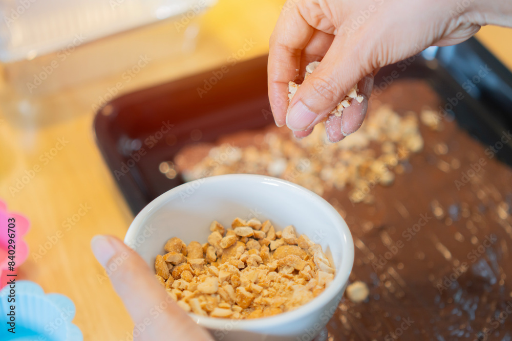 Female hand baker decorating tasty cake with cashew nuts at table. Homemade sweet concept.