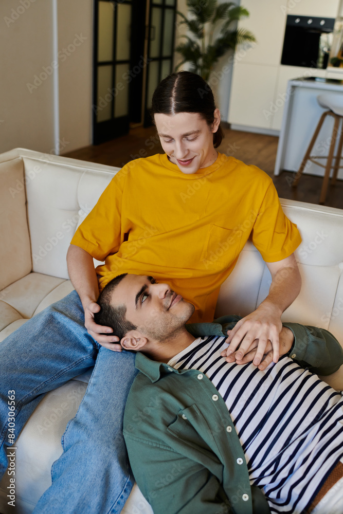 Fototapeta premium A young gay couple shares a tender moment of intimacy on a couch in a modern apartment.