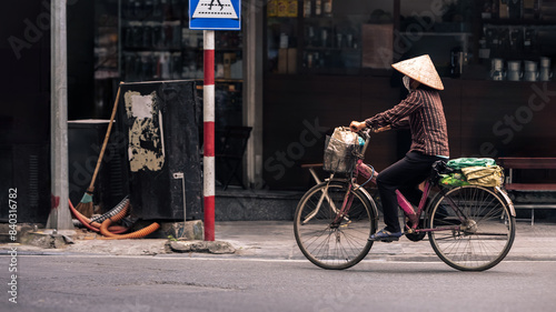 A Vietnamese woman street vendor wearing a traditional straw hat  pedals bicycle