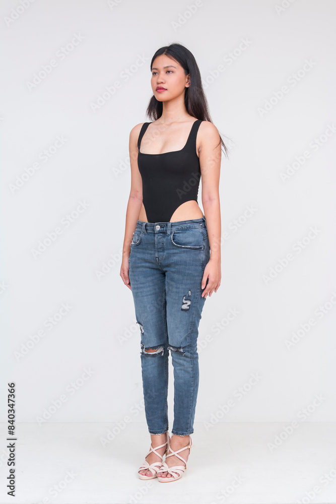 Angled view of a young asian woman of ideal height and figure in a black bodysuit and ripped jeans Isolated on a white background. Whole body photo. Angled view of a young asian woman of ideal height and figure in a black bodysuit and ripped jeans Isolated on a white background. Whole body photo.