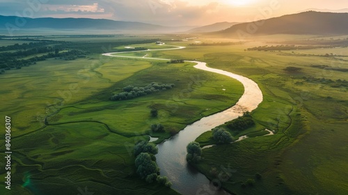 A drone shot of a meandering river through a lush green valley at sunrise