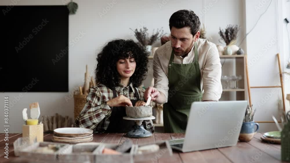 Two ceramists working on pottery together in bright workshop. Male and female artists focused on creating decorative clay piece. Two ceramists working on pottery together in bright workshop. Male and female artists focused on creating decorative clay piece.