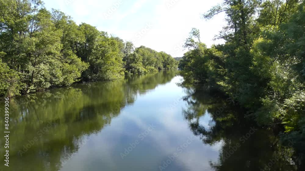 Video 4K, beautiful landscape of calm river with slowly flowing water and banks of green trees under sunlight with few clouds on blue sky Video 4K, beautiful landscape of calm river with slowly flowing water and banks of green trees under sunlight with few clouds on blue sky