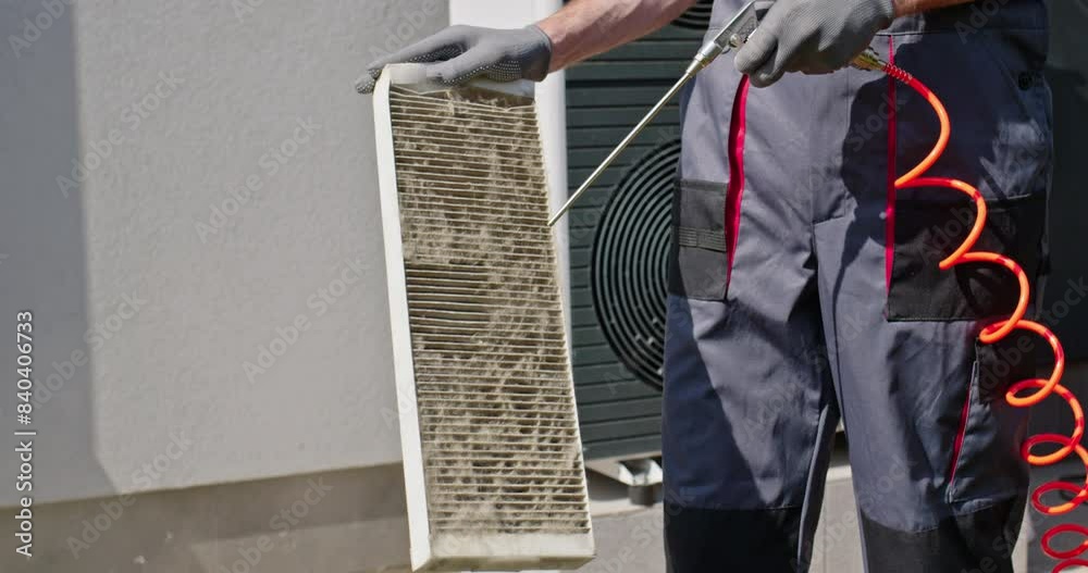 Worker cleaning a dirty air filter with a compressed air stream.