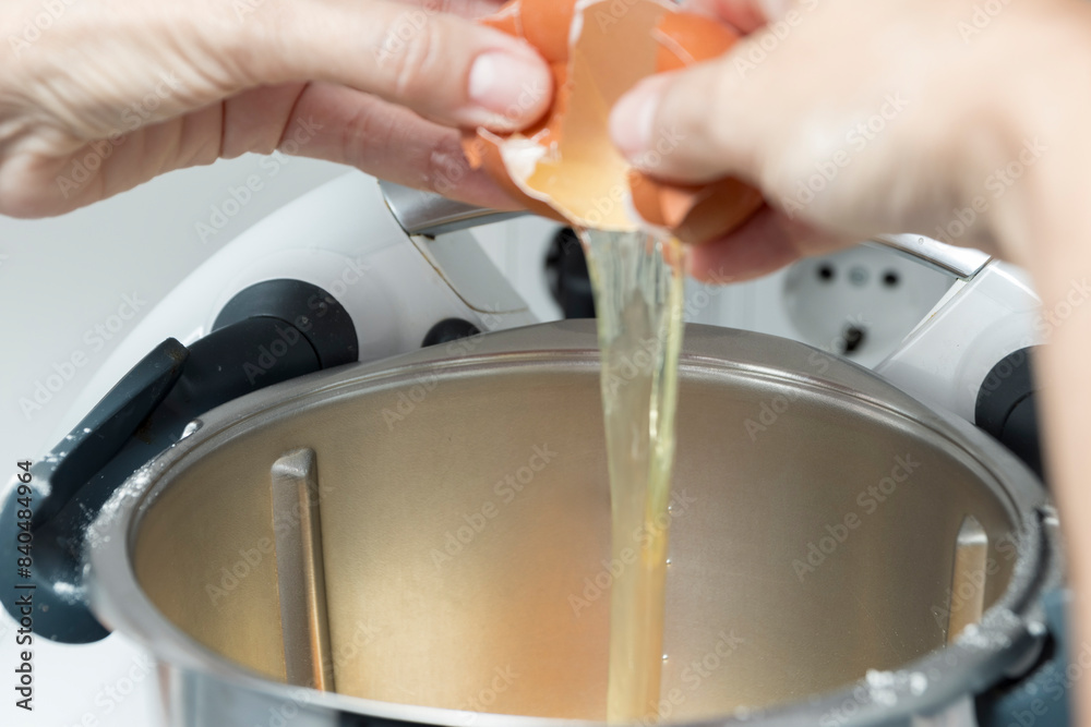 Hands cracking an egg into a mixer bowl for baking, white stand mixer, metallic bowl, focused on action Hands cracking an egg into a mixer bowl for baking, white stand mixer, metallic bowl, focused on action