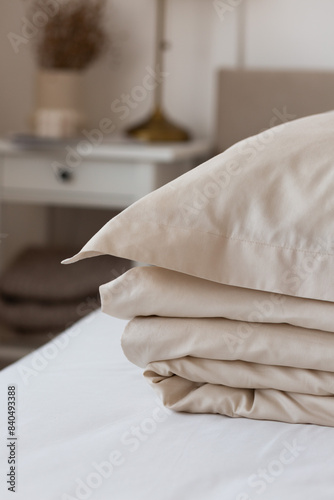 a stack of beige satin bed linen (satin, lyocell, silk): duvet cover and pillowcases with borders in a cozy interior. Cozy home concept. Home textiles