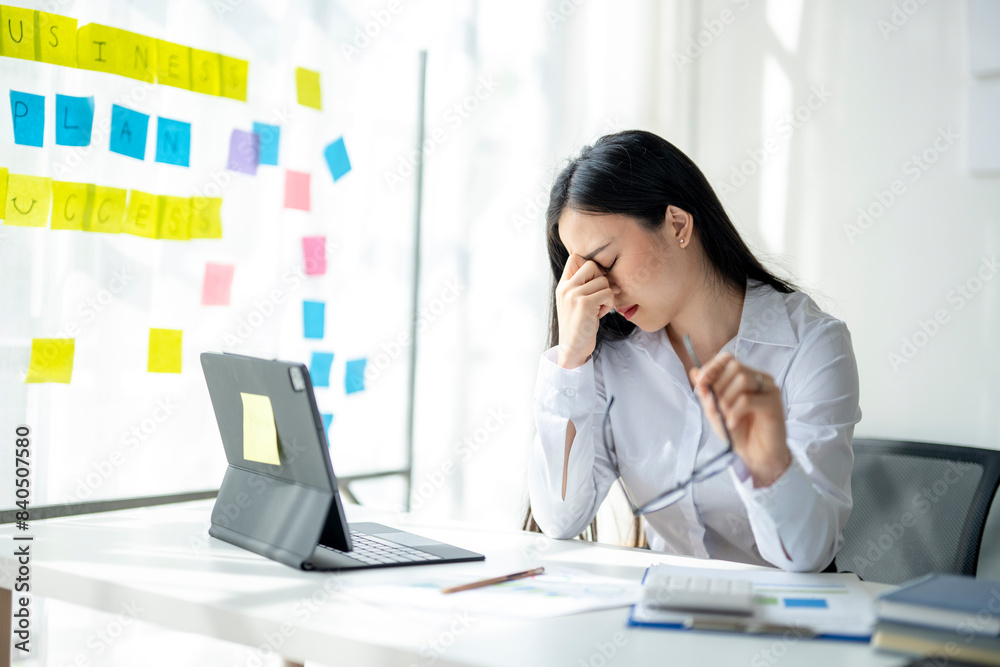 A woman is sitting at a desk with a computer and a stack of papers A woman is sitting at a desk with a computer and a stack of papers