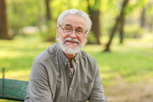 Portrait of happy grandpa with glasses on bench in park
