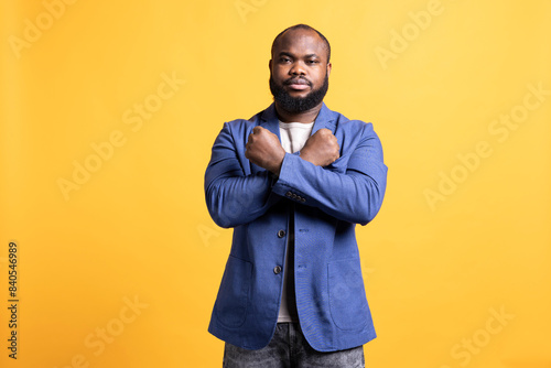 Assertive african american man showing letter X with arms crossed, staying in warrior stance, showing fierceness. Firm BIPOC person using negative body language to signal rejection, studio background