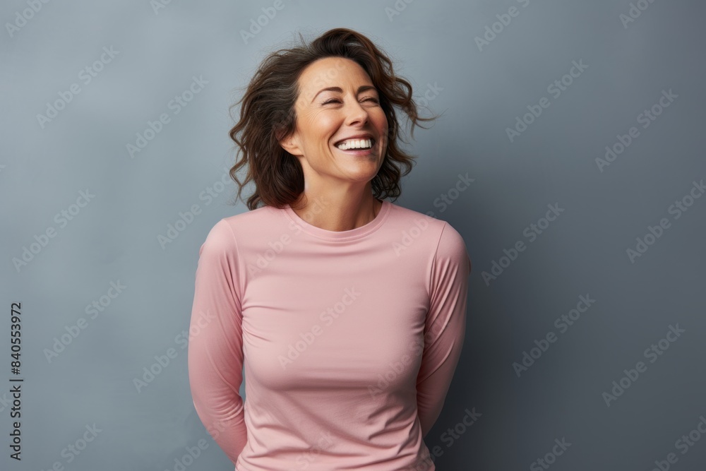 Portrait of a joyful woman in her 40s sporting a long-sleeved thermal undershirt in front of pastel gray background