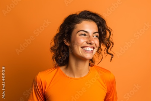 Portrait of a happy woman in her 20s sporting a breathable mesh jersey in front of soft orange background