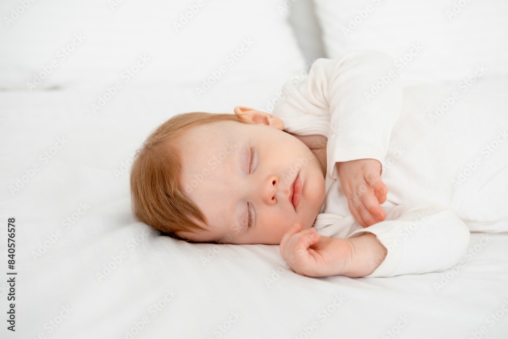 Baby boy sleeping under a blanket in a white bodysuit on the bed with his hand folded under his cheek, sweet healthy baby sleep at home Baby boy sleeping under a blanket in a white bodysuit on the bed with his hand folded under his cheek, sweet healthy baby sleep at home