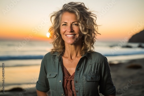 Portrait of a happy woman in her 50s wearing a rugged jean vest isolated on stunning sunset beach background