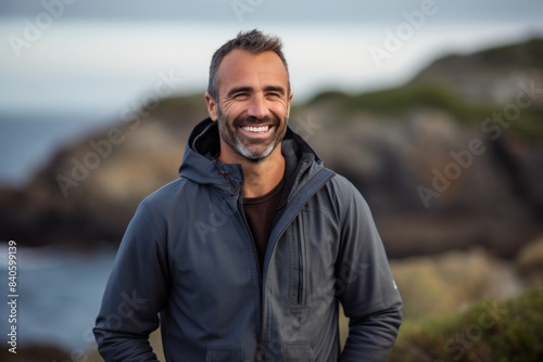 Portrait of a blissful man in his 40s sporting a stylish varsity jacket in front of rocky shoreline background