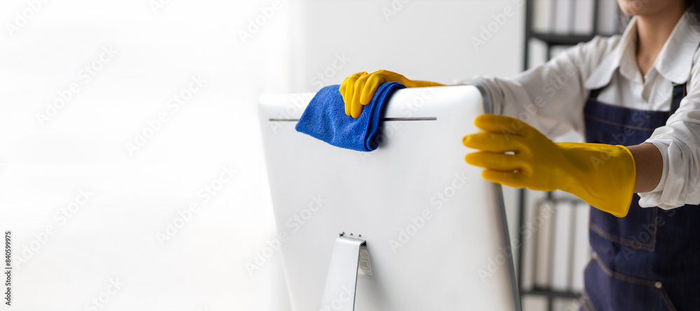 Young Asian cleaning woman uses a cloth to wipe clean a computer using cleaning solution in her home office. Young Asian cleaning woman uses a cloth to wipe clean a computer using cleaning solution in her home office.