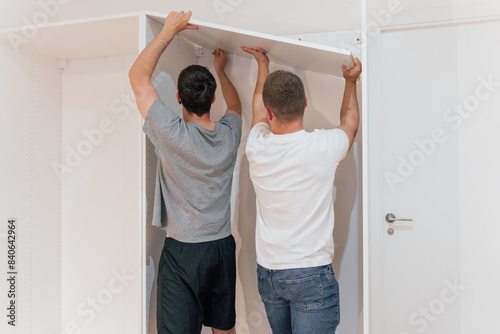 Obraz na plátně Two carpenters putting up a shelf to assemble a new cabinet