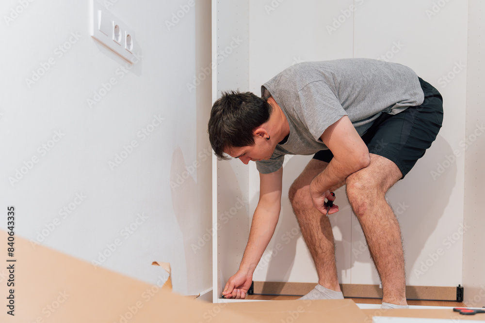 Young man bending over to assemble a closet in his new home. Furniture Concept Young man bending over to assemble a closet in his new home. Furniture Concept