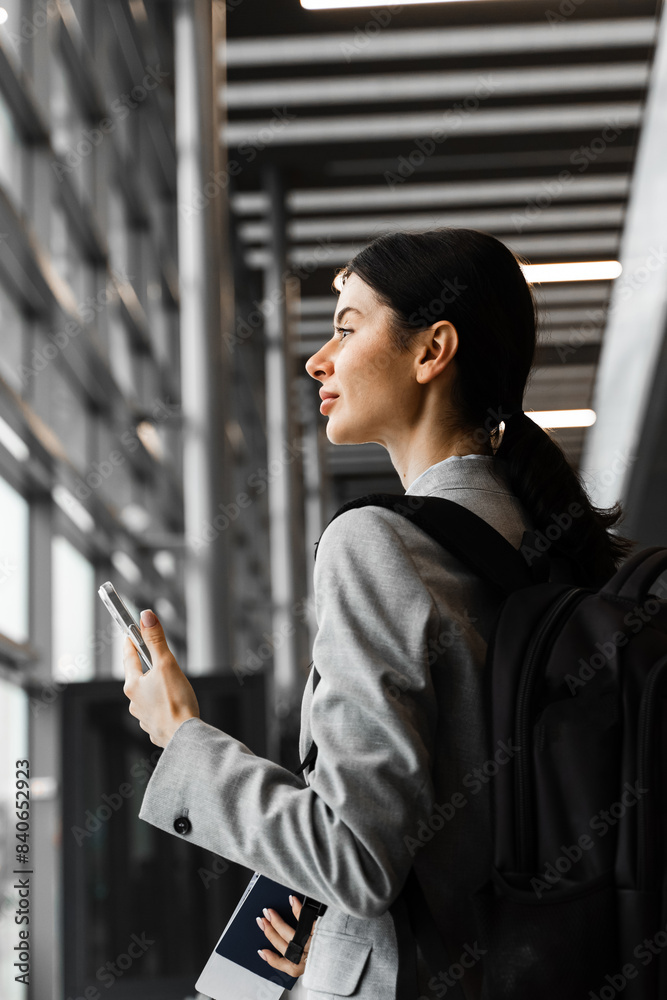Fototapeta premium Asian girl traveler with luggage heads towards boarding gate. Business woman with backpack and smartphone waiting for departure.