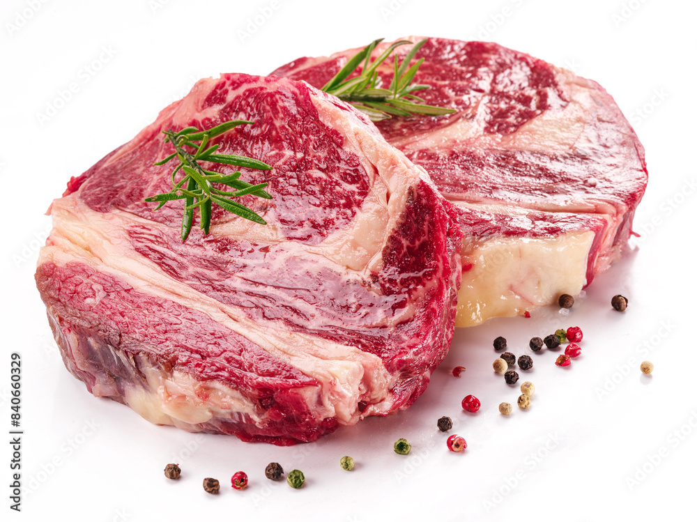 Obraz premium Raw beef steaks with herbs and spices ready for cooking on white background.