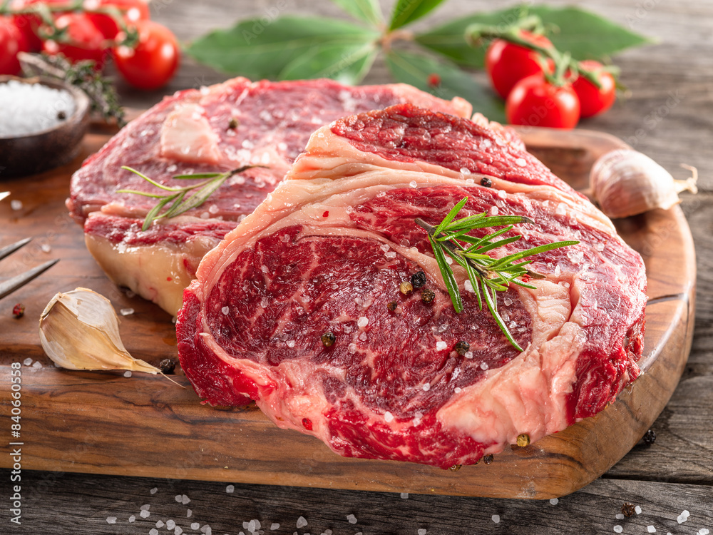 Raw beef steaks with herbs and spices ready for cooking are on wooden board. Raw beef steaks with herbs and spices ready for cooking are on wooden board.