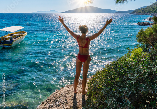 Woman in swimming suit is on the seashore, saluting the sun. Sun path sparkling in the calm water.