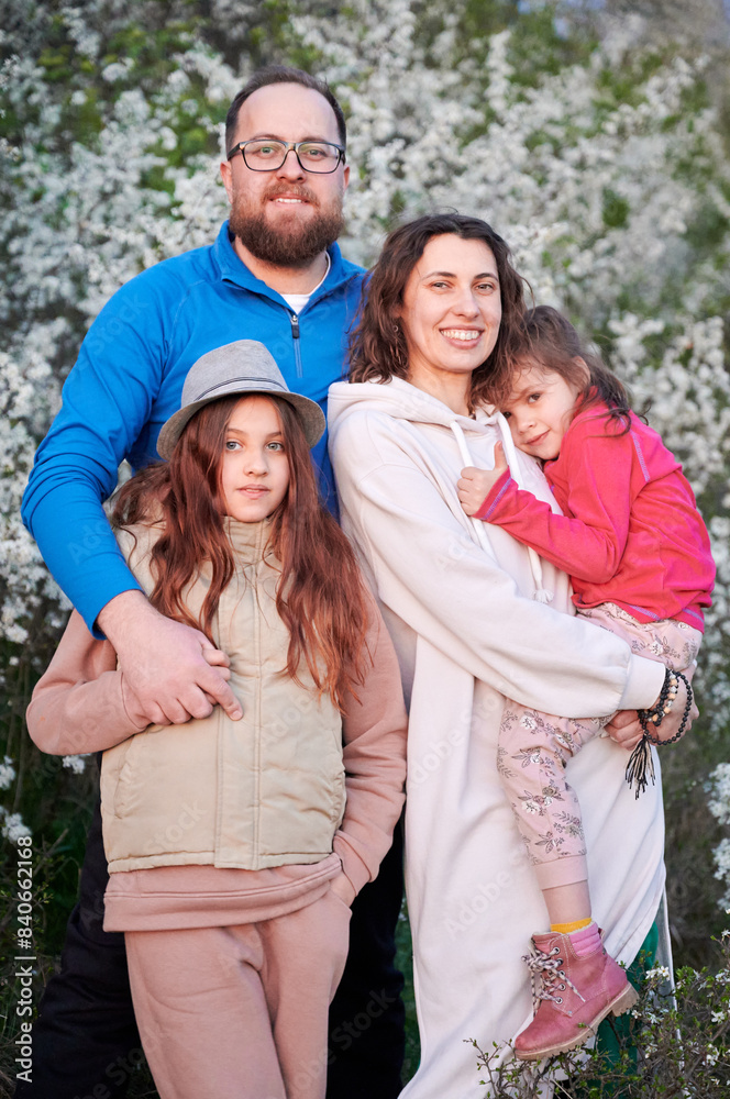 Fototapeta premium Family allergic enjoying after treatment from seasonal allergy at spring. Happy mother, father and two daughters smiling in front of blossom tree at springtime. Spring allergy concept.