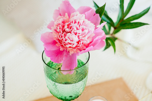 Bouquet of peonies in glass pink vase  green glass of water on the bed. Bedroom. Spring flowers.