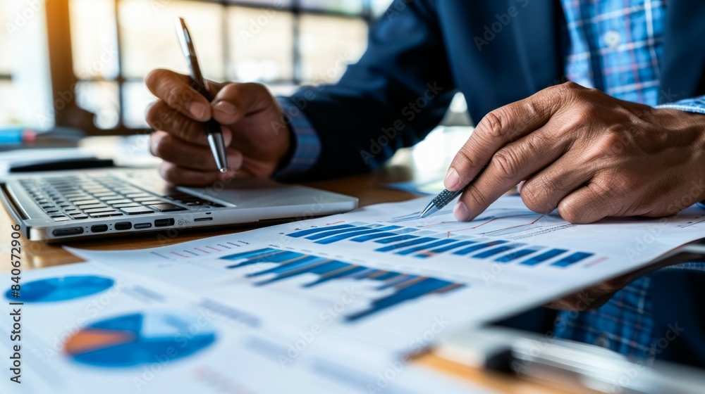Close-up of a persons hands reviewing financial data on a laptop and charts Close-up of a persons hands reviewing financial data on a laptop and charts