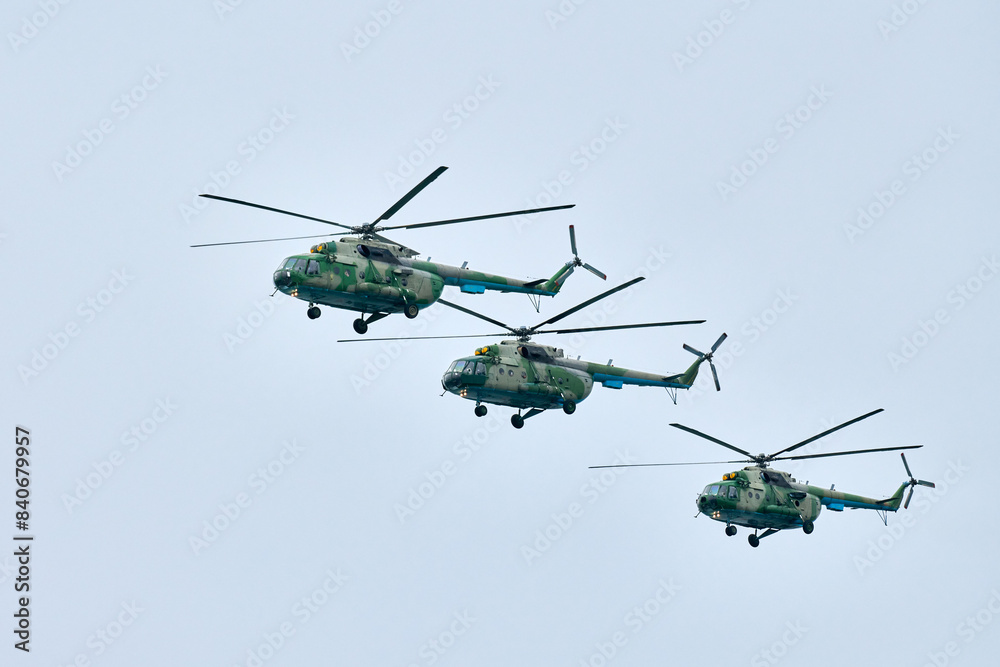 Fototapeta premium Three Russian military helicopters armed with missiles flies in blue sky, airborne mission of gunships with targeting system performs an aerial maneuvers for military operation, russian aviation