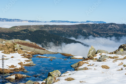 Mountain spring on the edge of snowy mountain on a sunny day overlooking Chartreuse and Belledonne mountain ranges covered in clouds in French alps