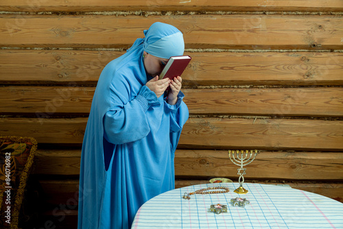 A Jewish woman in a blue veil at the table applies the siddur to her forehead photo