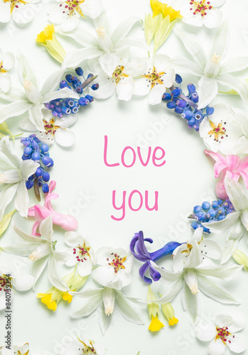 Colorful spring flowers arranged in a circular frame with Love you text in the center on a white background