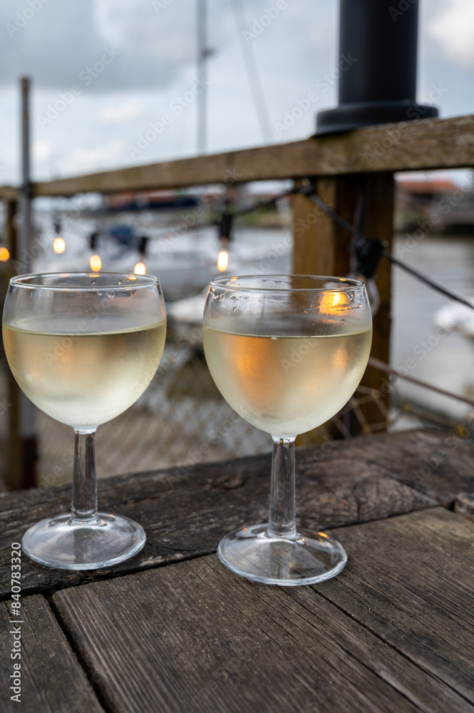 Obraz premium Tasting of Bordeaux white wine, right bank of Gironde Estuary, France. Glasses of white sweet French wine served in outdoor restaurant on oysters farm in Gujan-Mestras, Arcachon bay