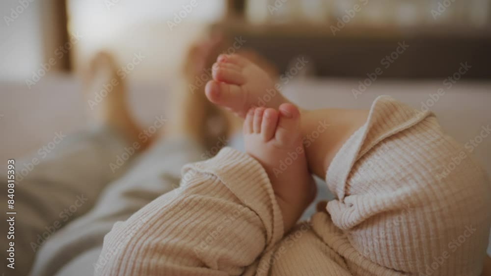 The couple is lying on the bed, their baby is in the middle of them. A small child tries to crawl by moving his legs. On a bright day, a family relaxes on the sofa. Parents raise their child with care