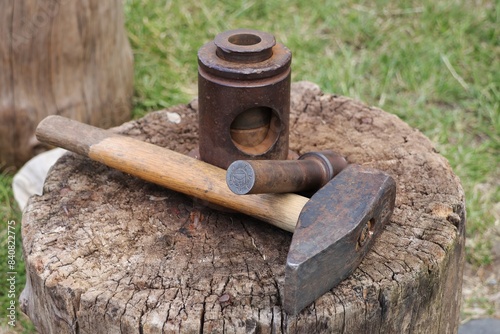 A hammer and a device for minting coins according to a medieval pattern lying on a wooden stump.