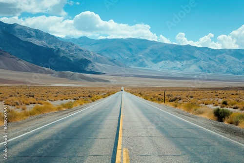 A solitary car drives down a long, straight road through a mountain pass.